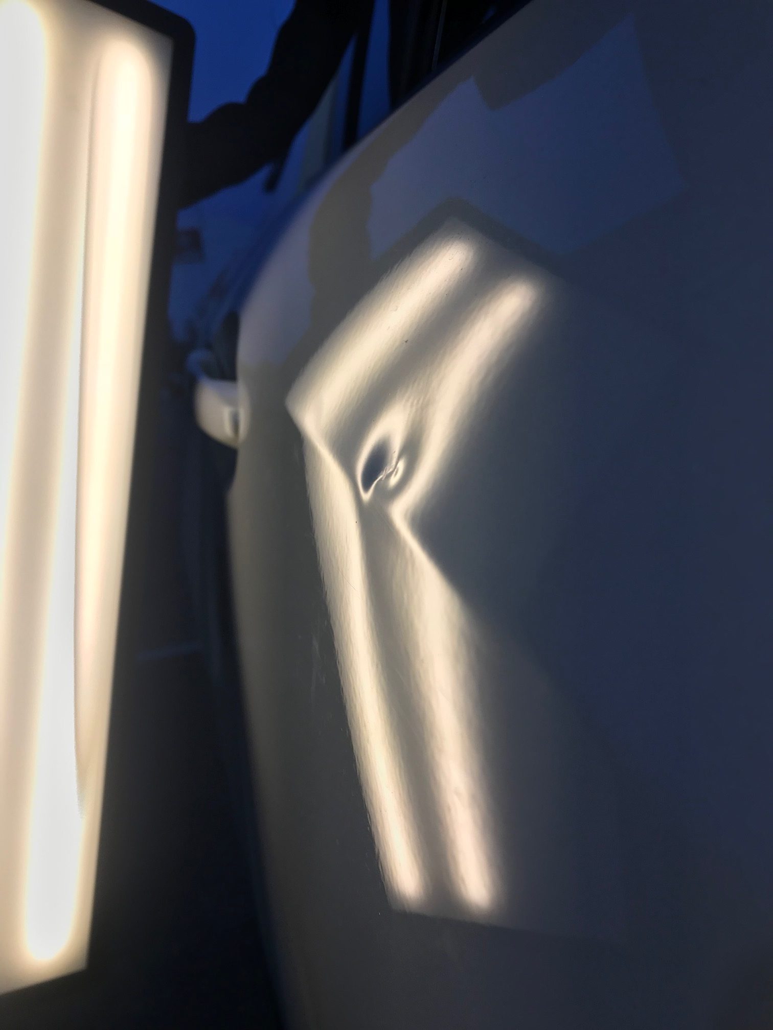 Before photo showing a sharp dent in a white vehicle door