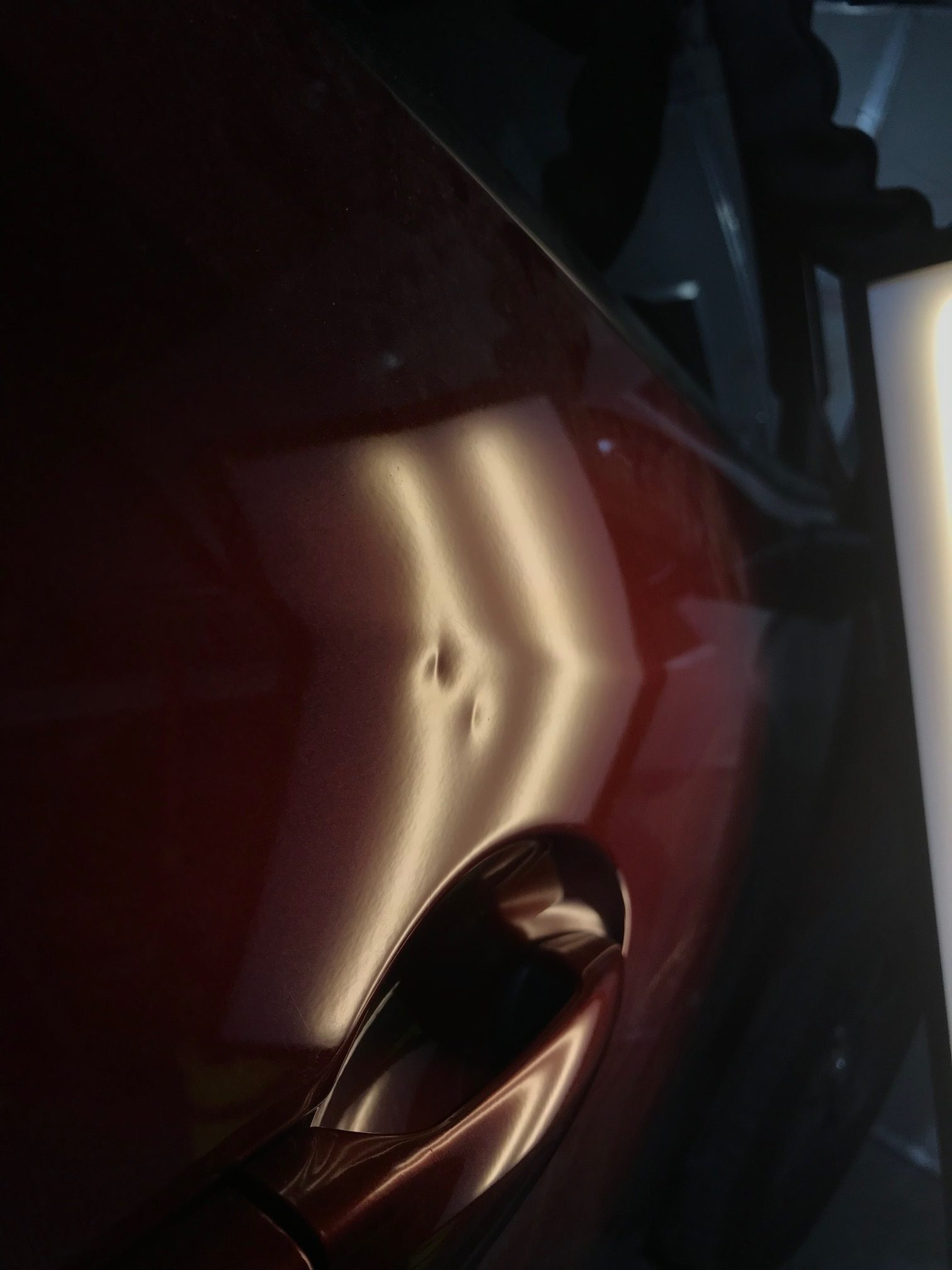 Before photo showing dents beside a red vehicle door handle