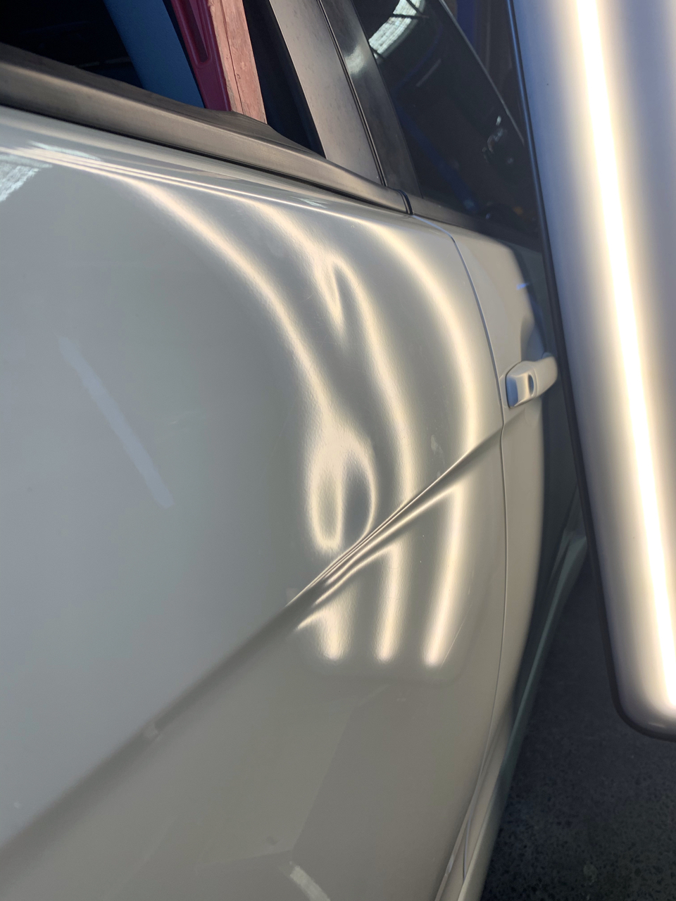 Before photo showing a dent in a white vehicle door