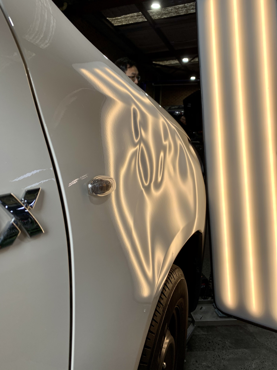 Before paintless dent repair on a white vehicle front guard at Dent X